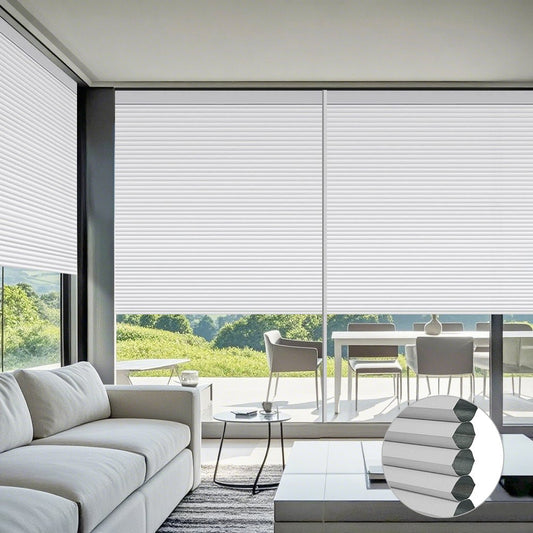 Motorized cellular shades in modern living room with white sofa, round side table, coffee cup, and large windows overlooking green landscape.