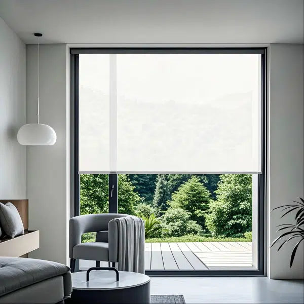Motorized light-filtering roller shade in modern bedroom with gray armchair, coffee table, and large window overlooking green garden