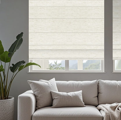 Motorized Roman shade in modern living room with light gray sofa, soft cushions, indoor plant, linen and window overlooking greenery